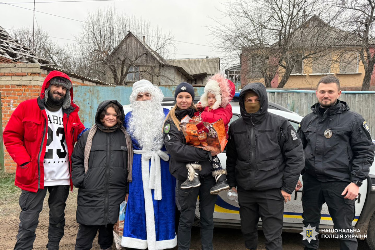 Поліцейські та Дід Мороз разом із дітьми під час зимового заходу.Поліцейський тримає дитину з подарунком, поруч Дід Мороз.