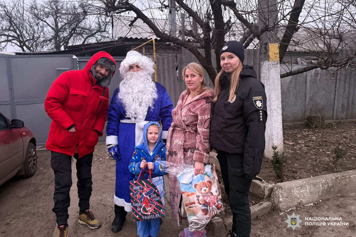 Поліцейський, Дід Мороз та родина з дітьми стоять біля житлового будинку; у руках святкові пакети з подарунками.