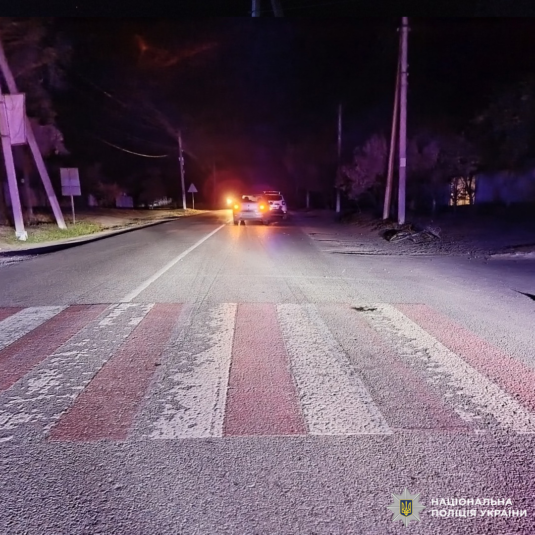 Нічна дорога з червоно‑білим пішохідним переходом, далі видно поліцейські автомобілі з увімкненими фарами.