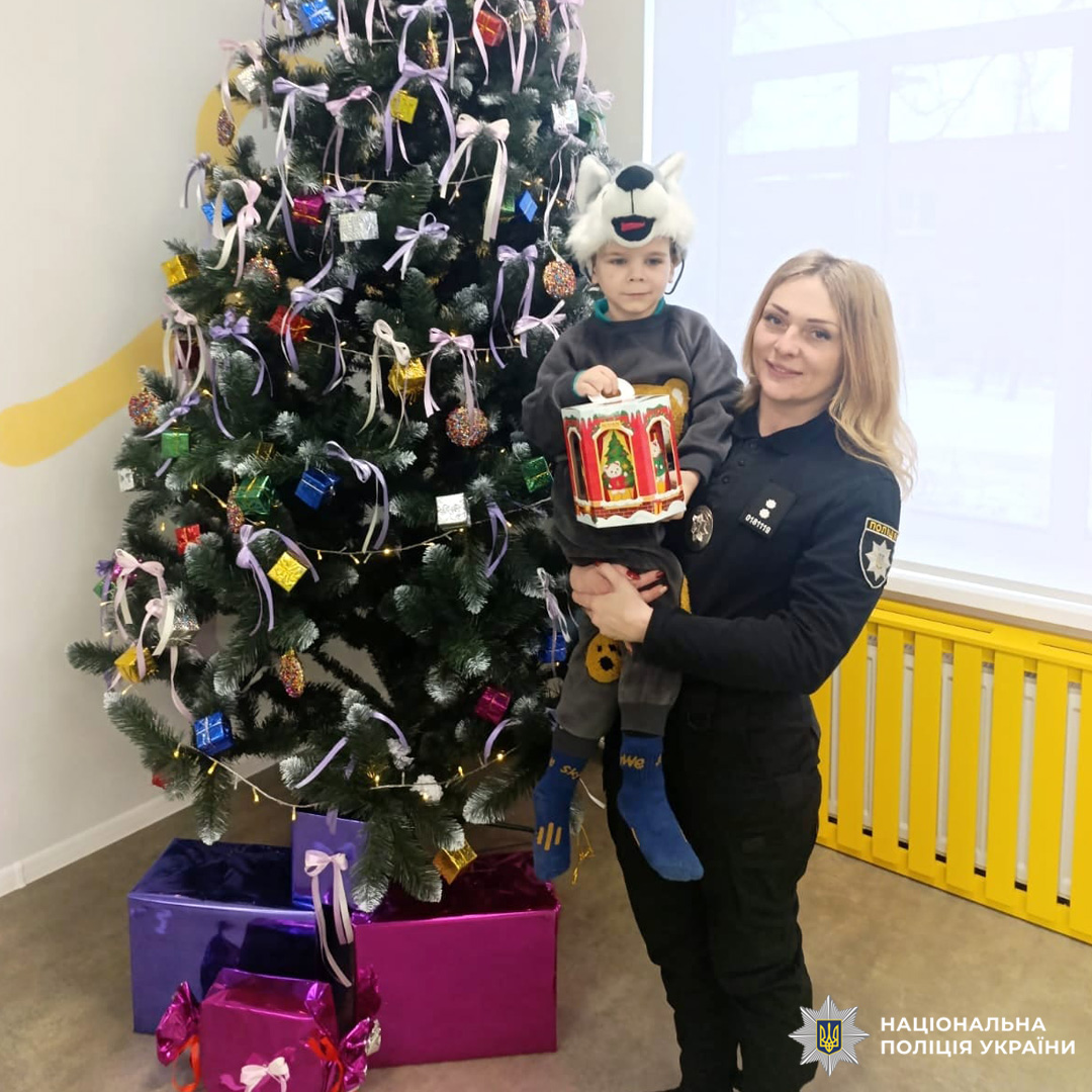 Поліцейська тримає дитину у святковому костюмі біля ялинки.