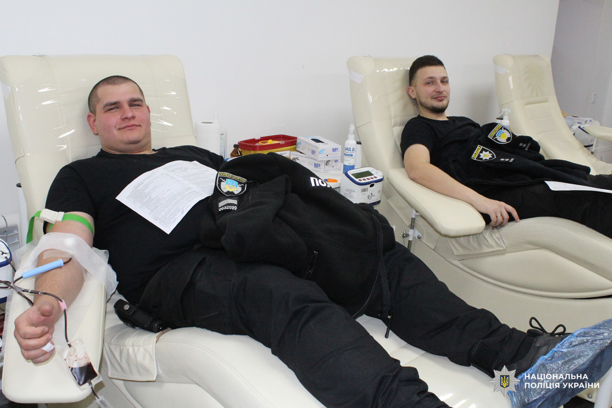 Поліцейський здають кров у клінічному приміщенні; видно апарати для збору крові та медичні матеріали.