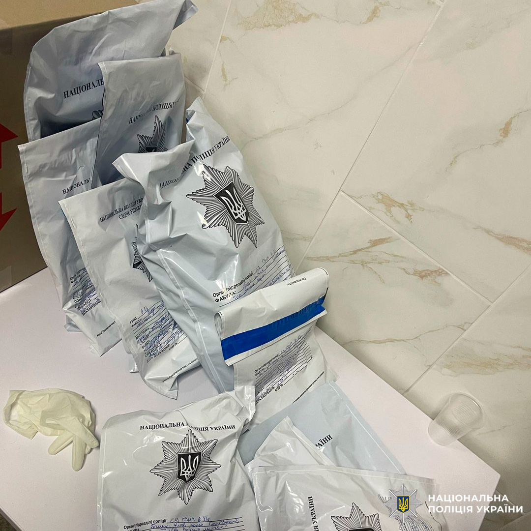 Запечатані пакети з маркуванням Національної поліції України, задокументовані на столі разом із рукавичками та пластиковим стаканом.