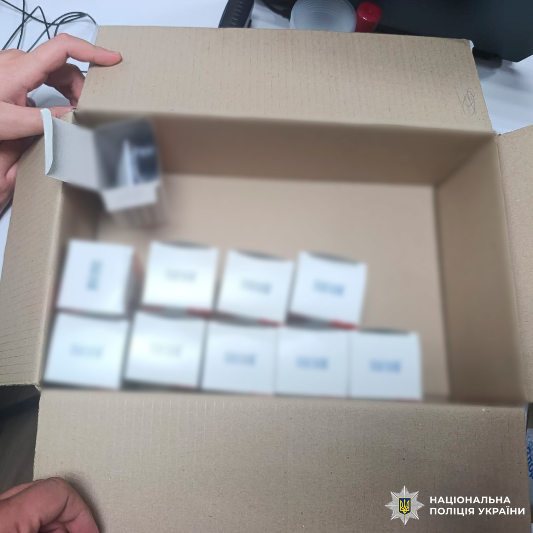 Картонна коробка з білими упаковками зі штрих‑кодами, одна з яких відкрита й містить круглі предмети.