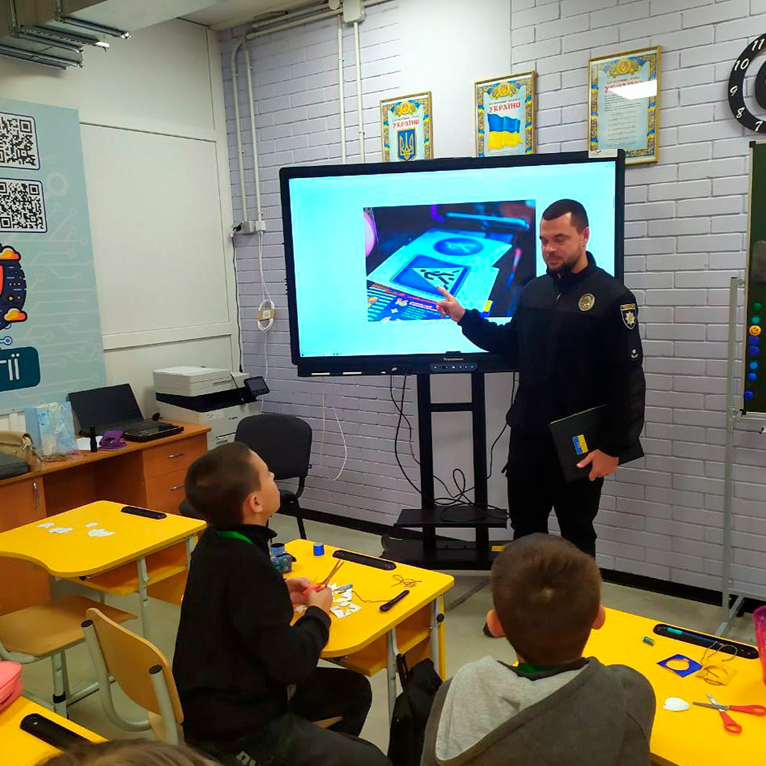 Учні слухають лекцію представника Національної поліції України у сучасному класі з цифровим екраном.