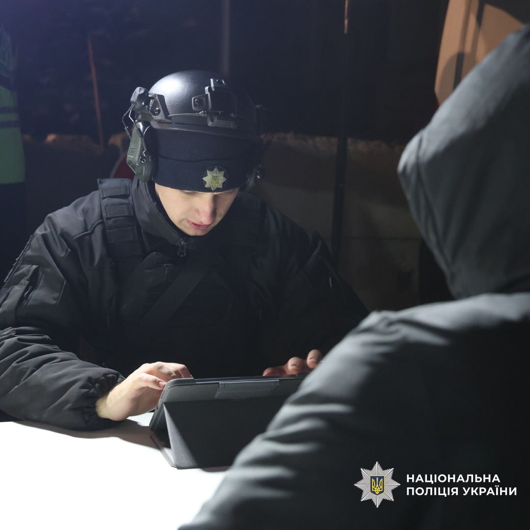 Поліцейський у спорядженні працює з планшетом уночі.