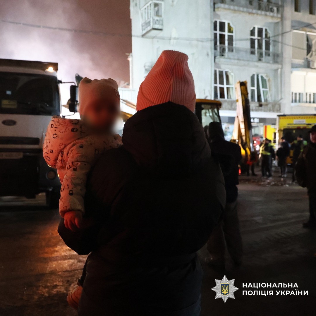 Жінка тримає дитину на місці надзвичайної події вночі.