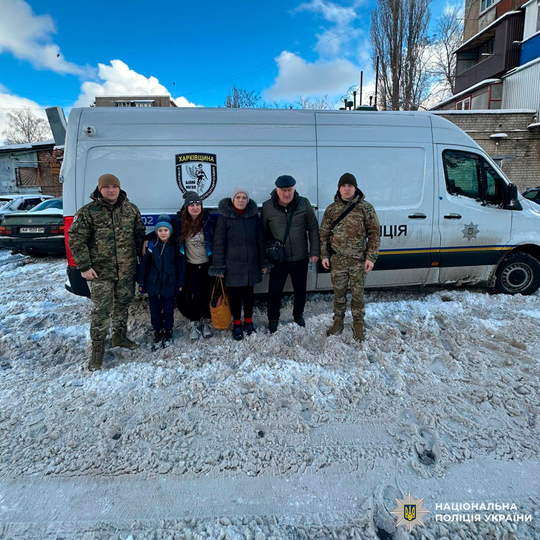 Шестеро людей стоять біля поліцейського мікроавтобуса Харківщини на засніженій вулиці.