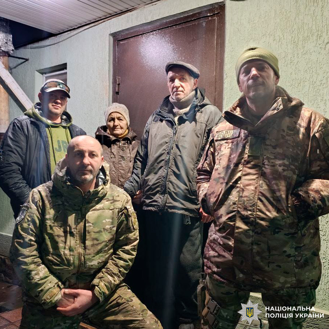 Шестеро людей - двоє у поліцейських та четверо у цивільному зимовому одязі - біля входу до будівлі вночі.