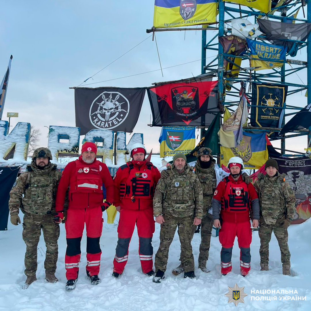 Група поліцейських та рятувальників Червоного Хреста стоїть разом на снігу перед прапорами та банерами.