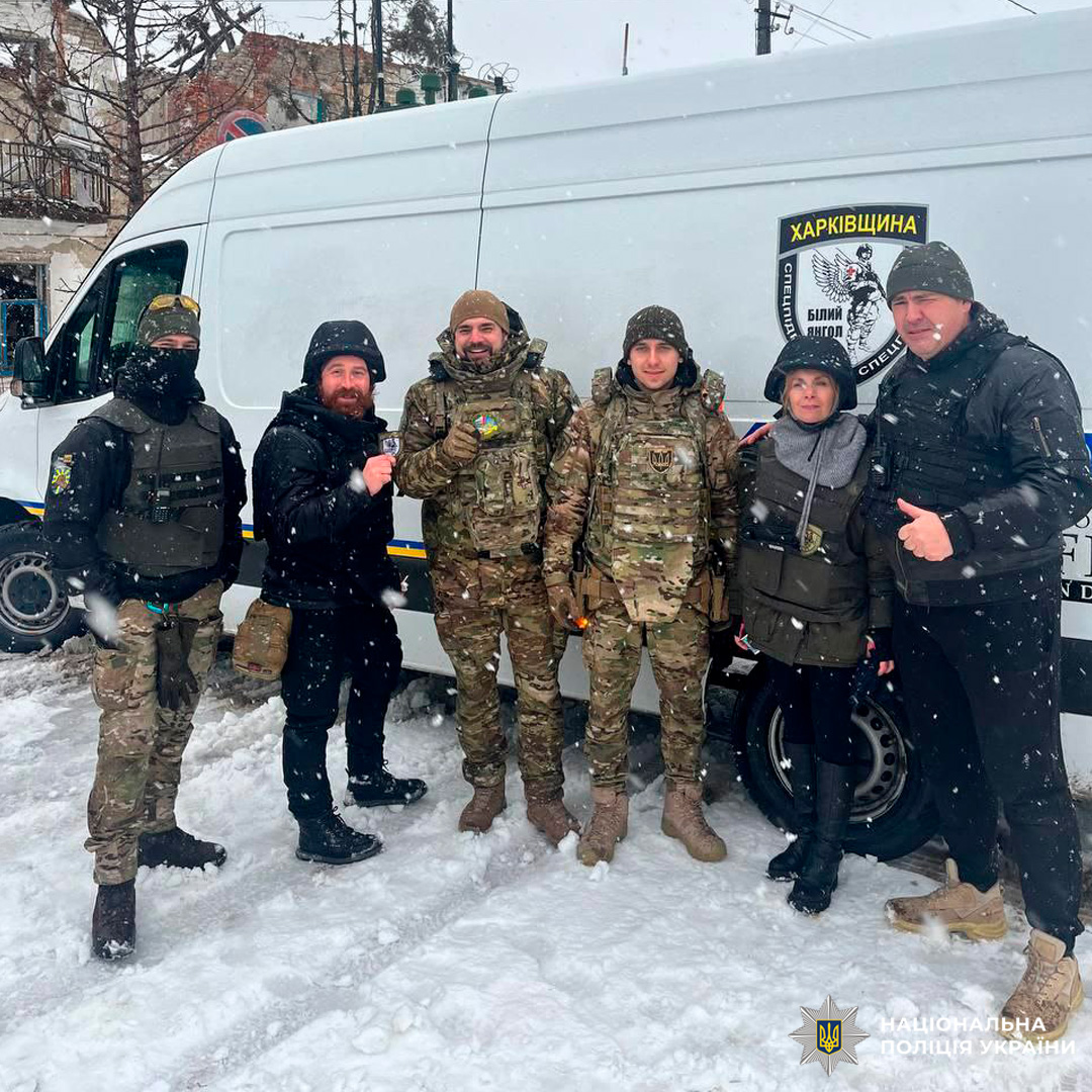 Шестеро людей стоять біля поліцейського мікроавтобуса Харківщини на засніженій вулиці.