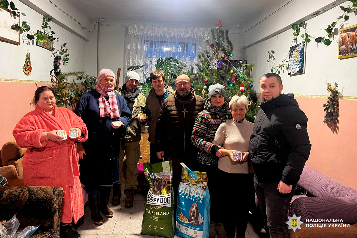 Група співробітників Національної поліції України стоїть у приміщенні, прикрашеному до Різдва. Поруч із ними великі пакети корму для собак.