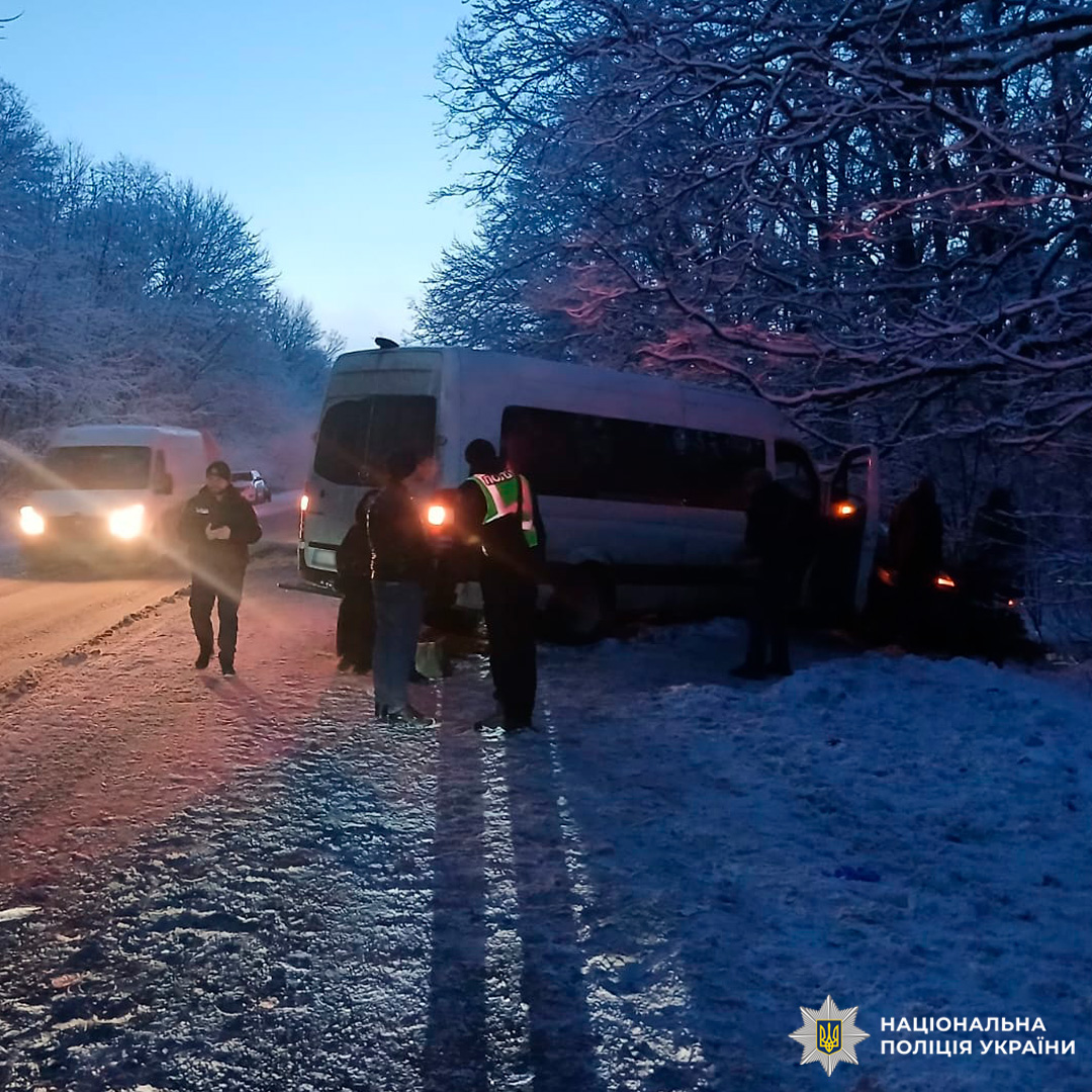 На засніженій дорозі видно мікроавтобус, що з’їхав у лісосмугу. Поруч працюють кілька поліцейських. Інший автомобіль стоїть на узбіччі з увімкненими фарами.