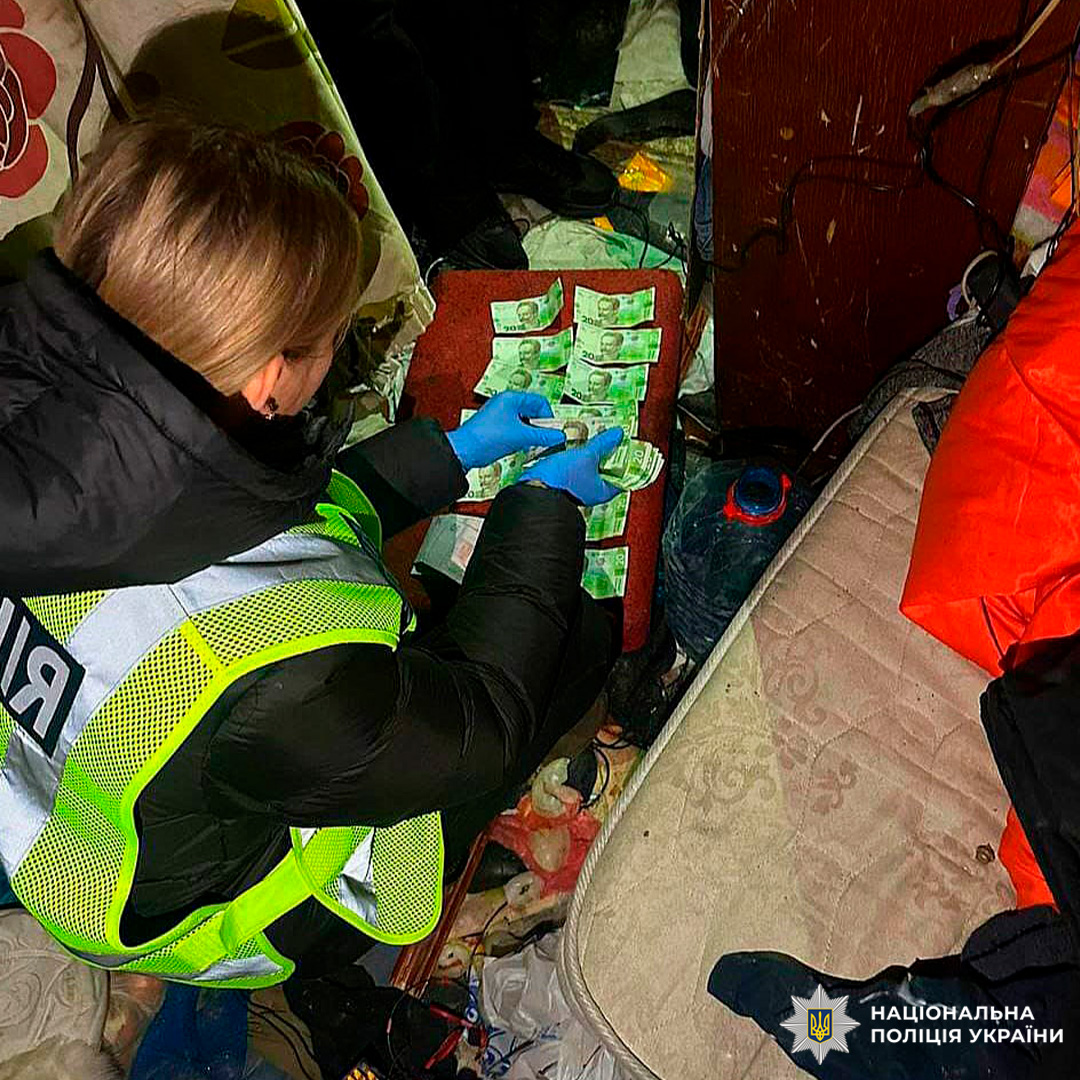 Поліцейський у світловідбивному жилеті оглядає українські банкноти, розкладені на столі.