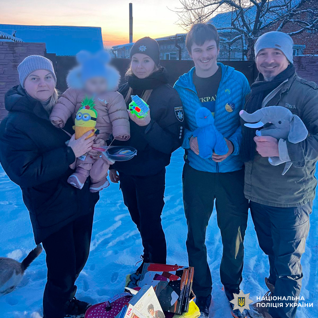 Поліцейські та дорослі з дитиною тримають іграшки й книги на засніженій місцевості.