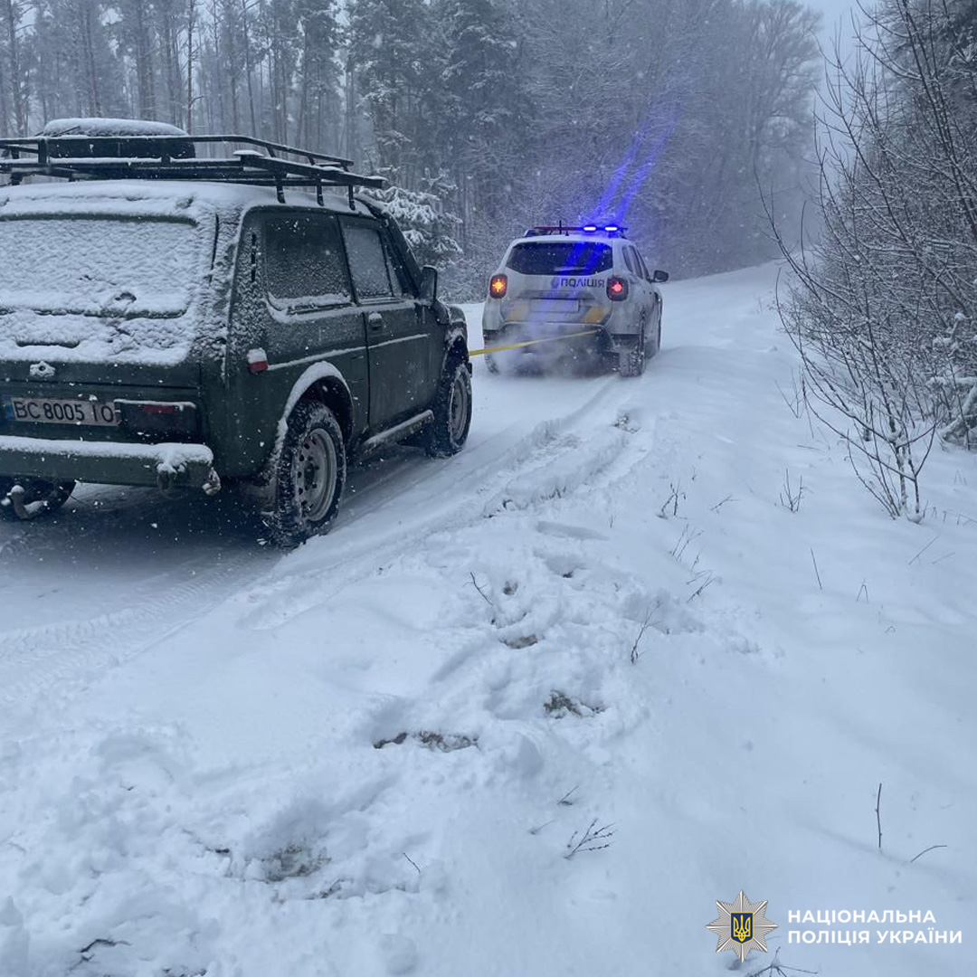 Поліцейський позашляховик буксирує інший автомобіль засніженою дорогою.