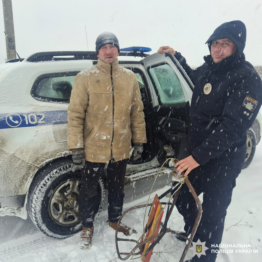 Поліцейський у формі тримає санчата, поруч цивільний у зимовому пальті; позаду службове авто.