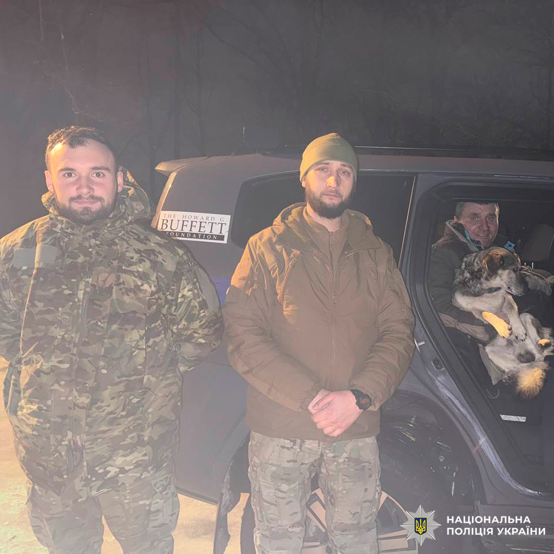 Люди у камуфляжі біля автомобіля; один у салоні тримає спокійного собаку.