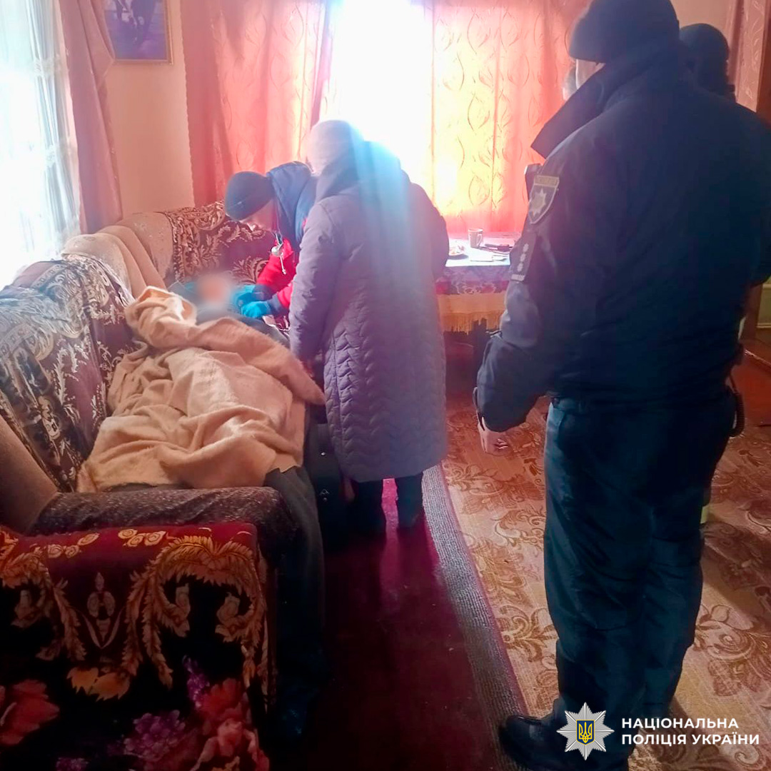 Поліцейські та цивільні надають допомогу людині, яка лежить на дивані у житловому приміщенні.