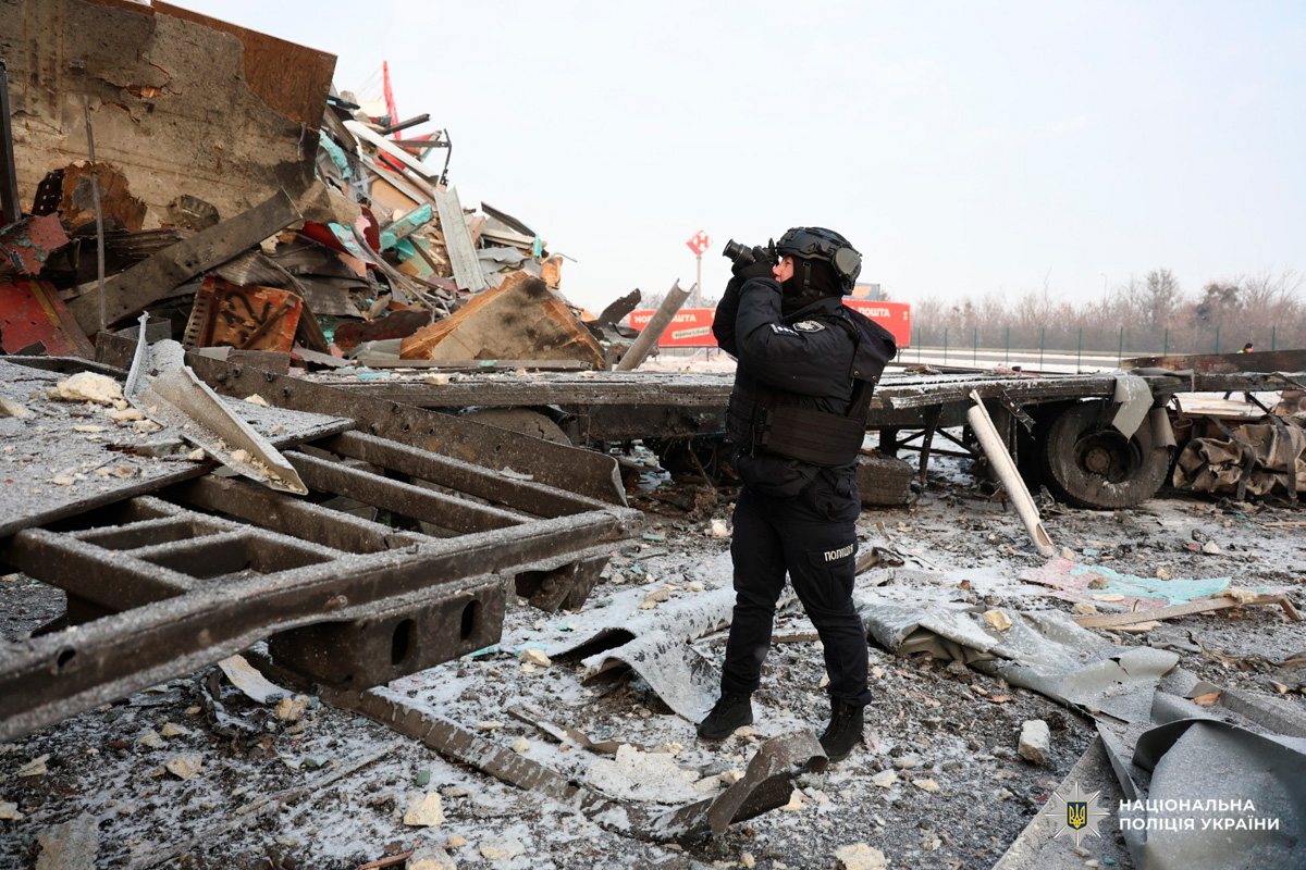 Співробітник поліції у тактичному спорядженні здійснює фотозйомку місця руйнувань.