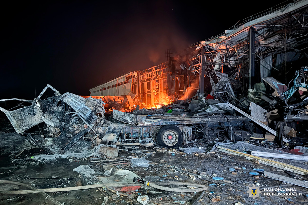 Зруйнована будівля у вогні, поруч уламки та згорілий автомобіль.