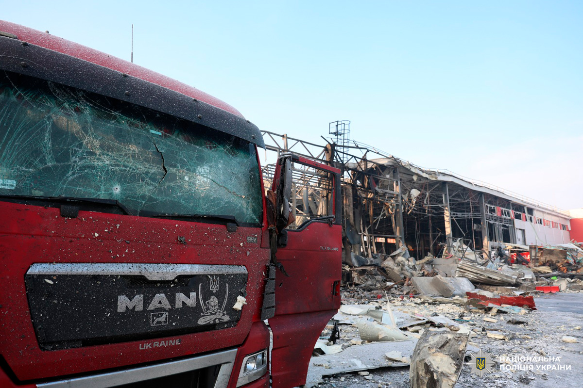 Червона вантажівка MAN пошкоджена уламками біля зруйнованої будівлі.