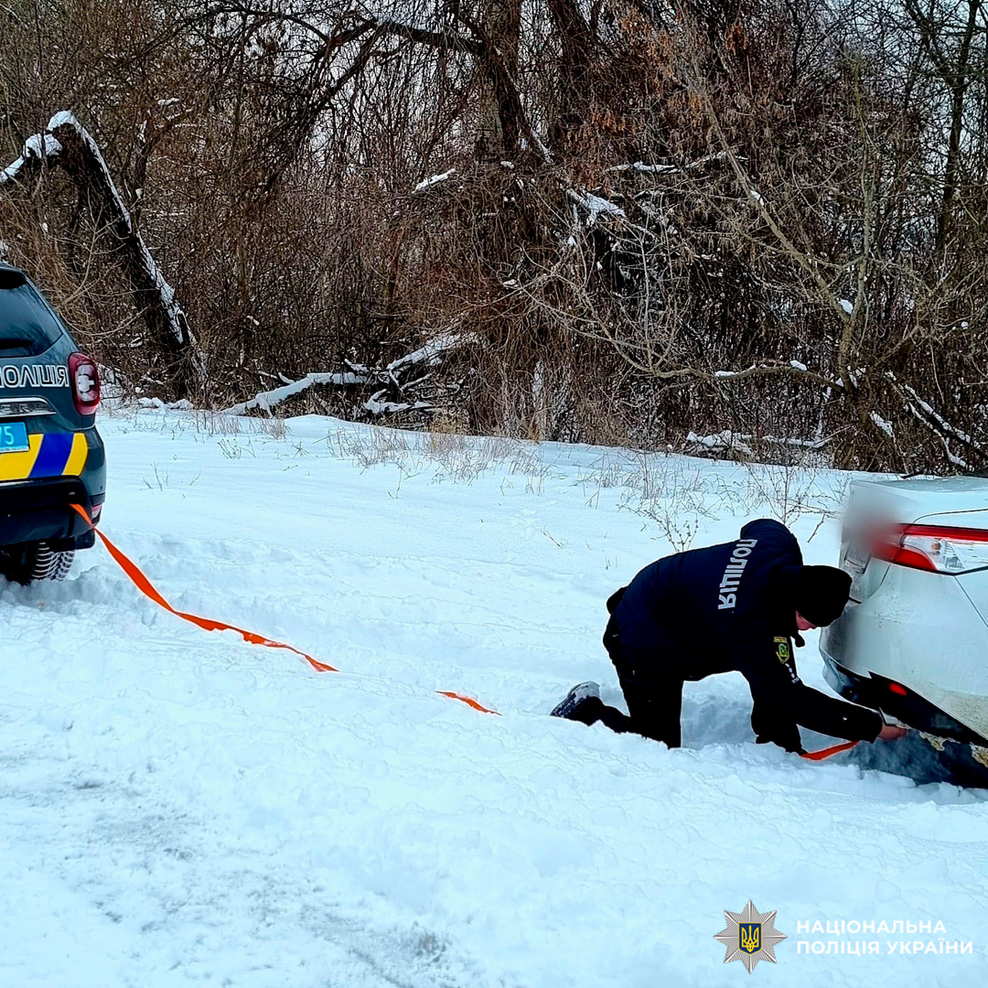 Поліцейський надає допомогу водію, буксируючи автомобіль, що застряг у снігу.