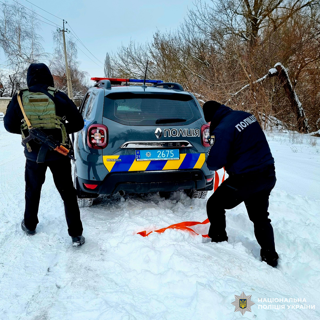 Поліцейський надає допомогу водію, буксируючи автомобіль, що застряг у снігу.