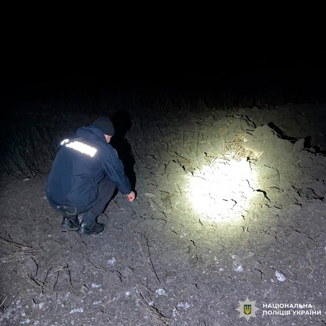 Поліцейський оглядає місце події, освітлюючи тріщини на землі ліхтарем у нічний час.