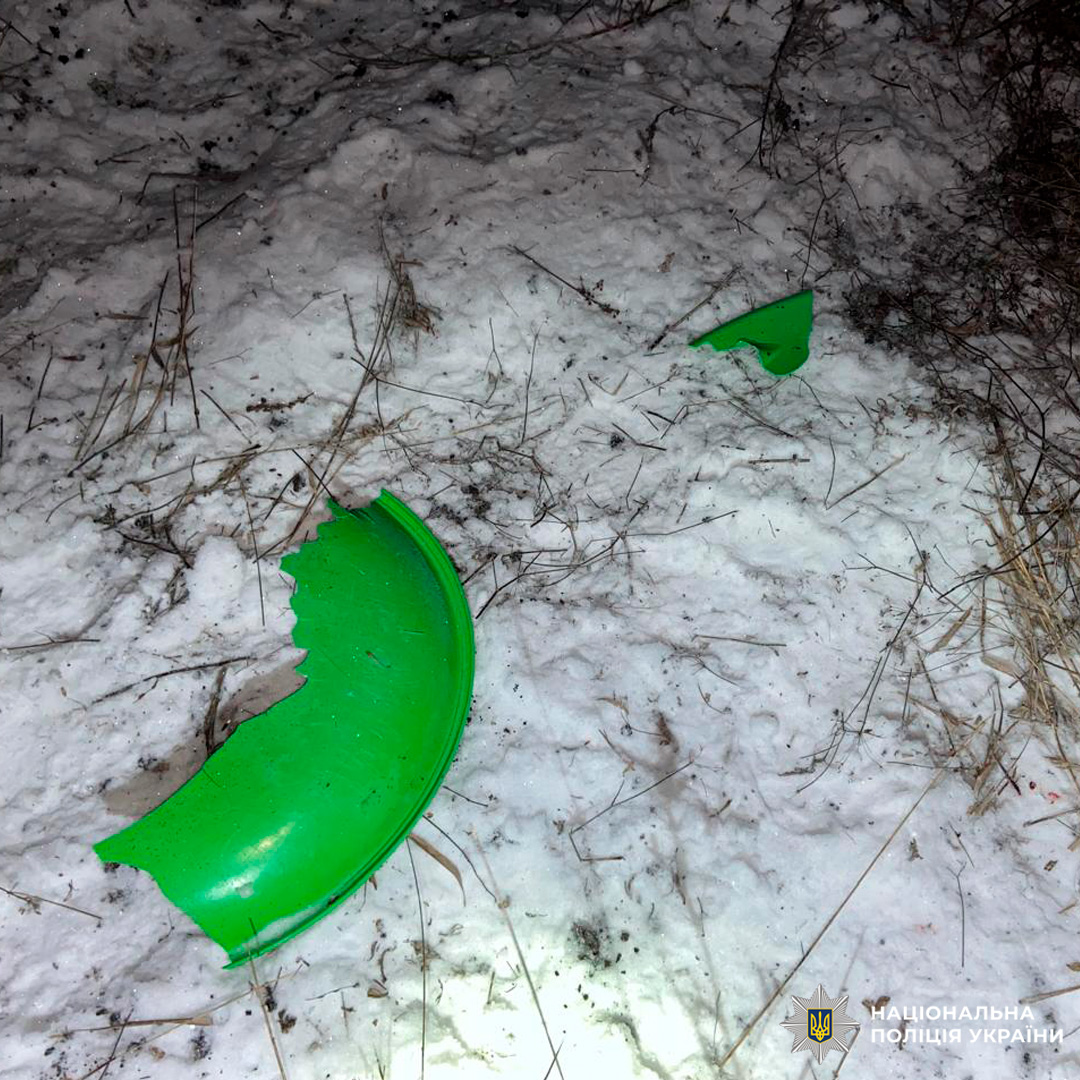 Зламані частини зелених санок лежать на снігу.