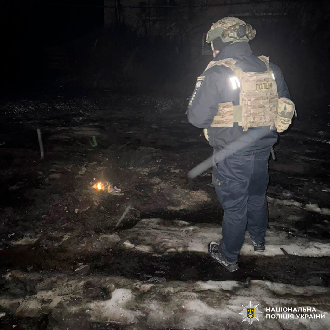 Поліцейський оглядає місце події, освітлюючи тріщини на землі ліхтарем у нічний час.