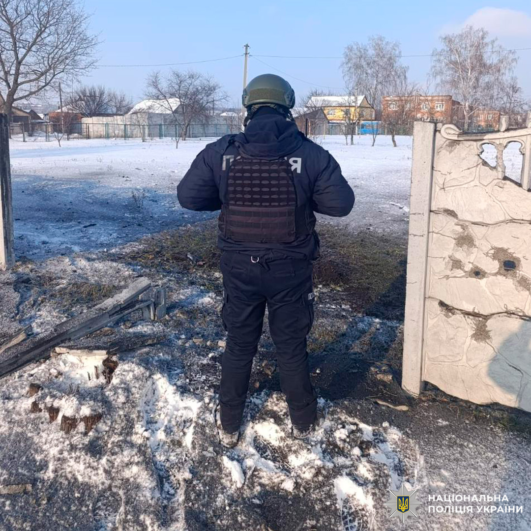 Поліцейський у тактичному спорядженні оглядає місце події біля пошкодженої бетонної стіни в зимових умовах.