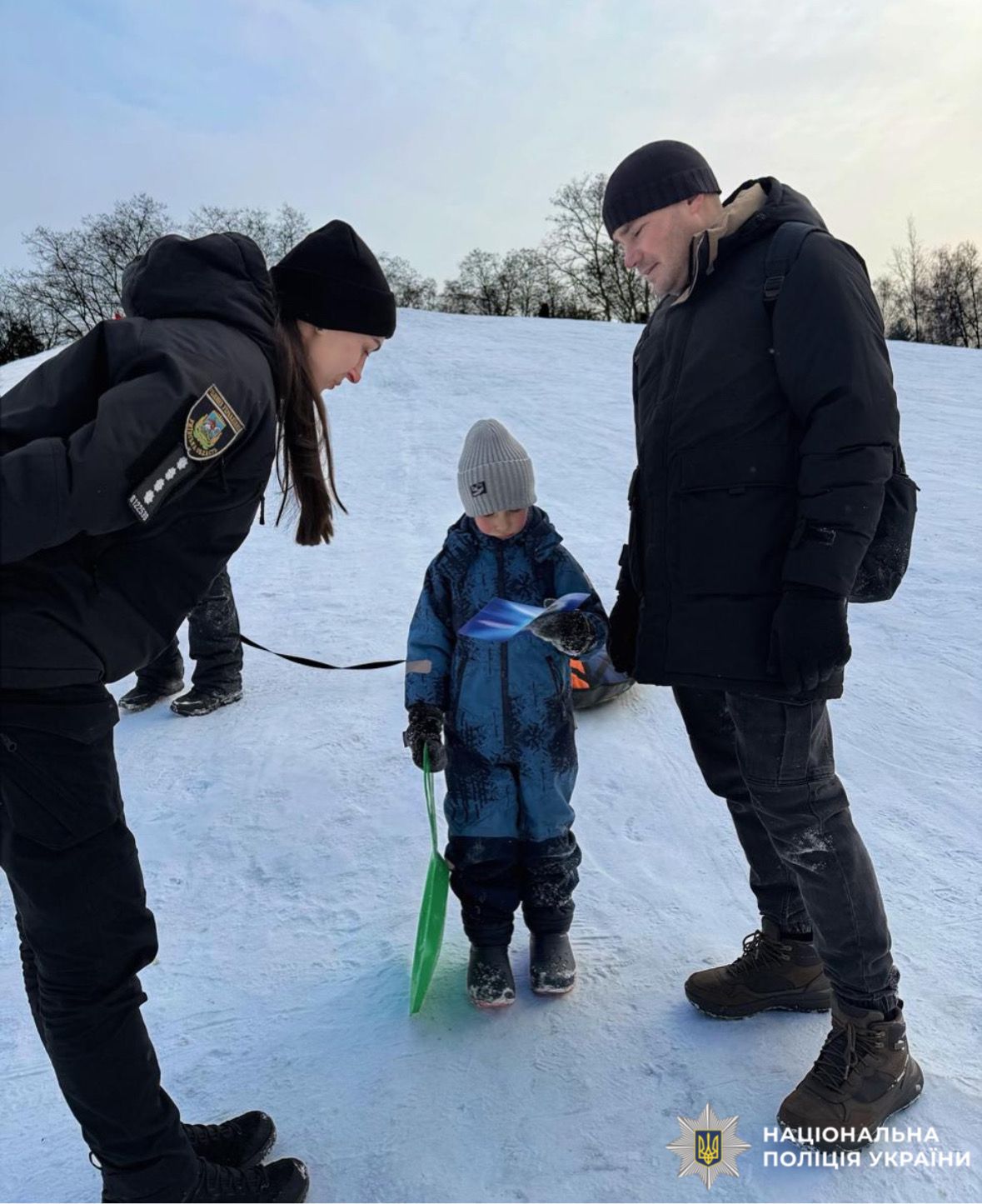 На фотографії зображено ювенальну поліцейську, яка проводить профілактичний захід з дітьми поблизу зимових водойм.