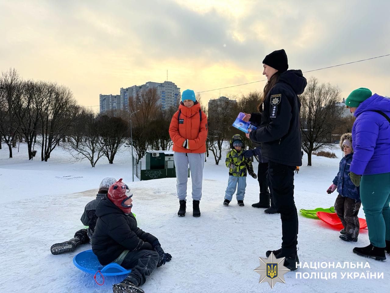 На фотографії зображено ювенальну поліцейську, яка проводить профілактичний захід з дітьми поблизу зимових водойм.