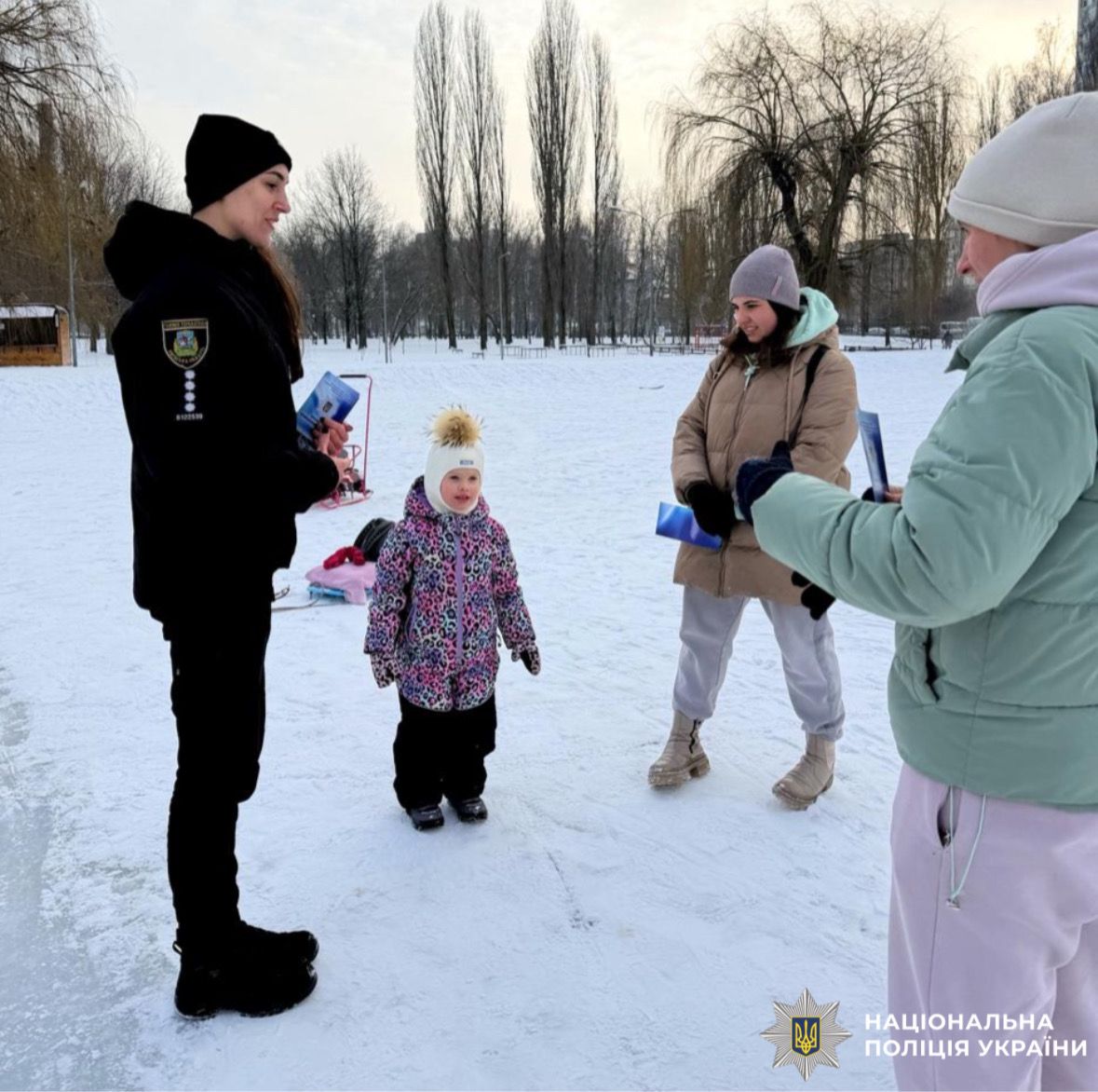 На фотографії зображено ювенальну поліцейську, яка проводить профілактичний захід з дітьми поблизу зимових водойм.