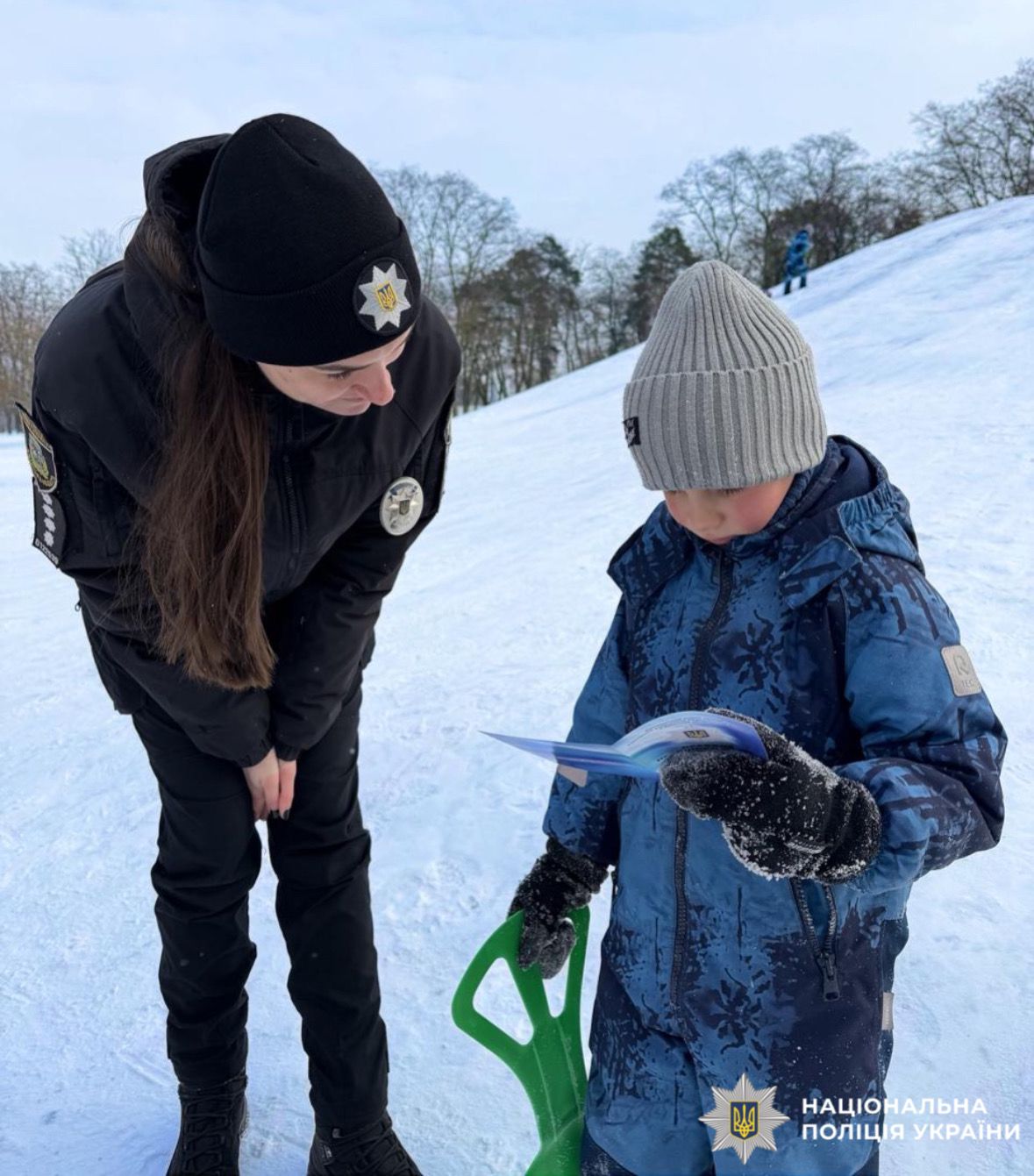 На фотографії зображено ювенальну поліцейську, яка проводить профілактичний захід з дітьми поблизу зимових водойм.