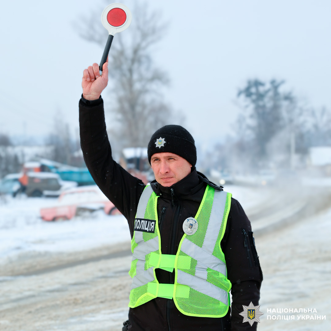 Поліцейський регулює рух транспорту на засніженій дорозі, використовуючи червоний сигнальний диск.