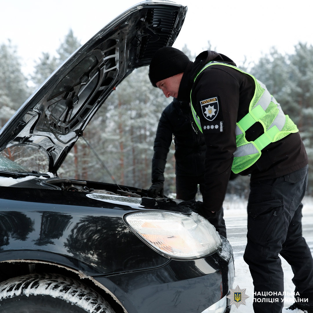 Поліцейський оглядає двигун автомобіля на засніженій дорозі.