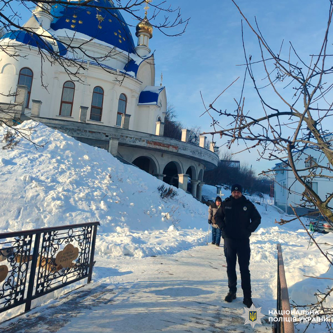 Поліцейський у тактичному спорядженні біля храму взимку.
