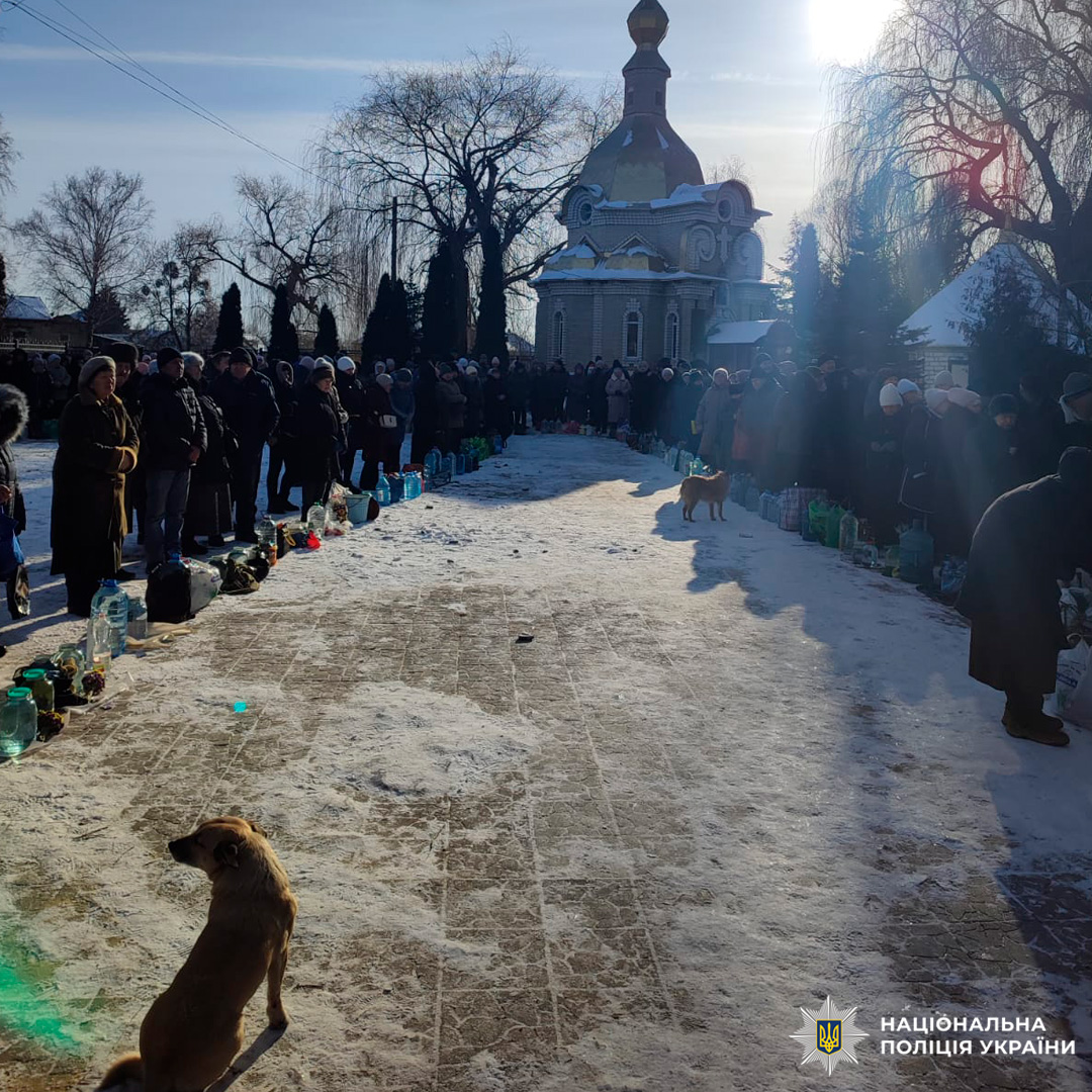 Люди з ємностями для води стоять уздовж засніженої доріжки біля храму.
