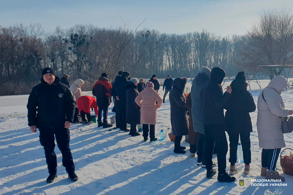 Громада біля водойми взимку, поліцейський забезпечує порядок.