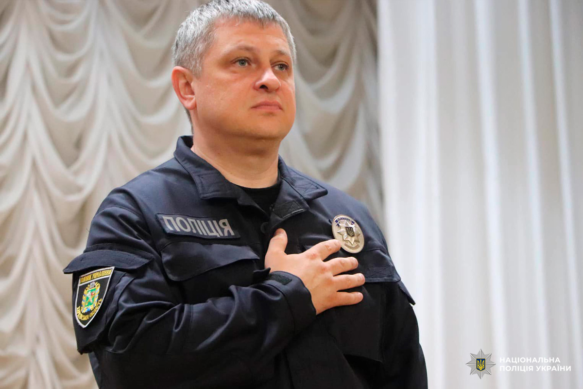 Офіцер Національної поліції України стоїть у формі з рукою на серці.