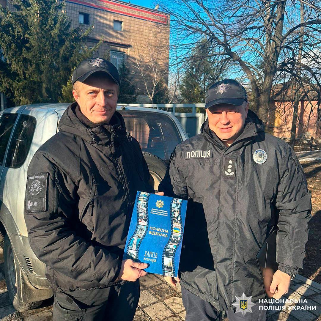 Двоє офіцерів Національної поліції України стоять на вулиці, один тримає почесну відзнаку.