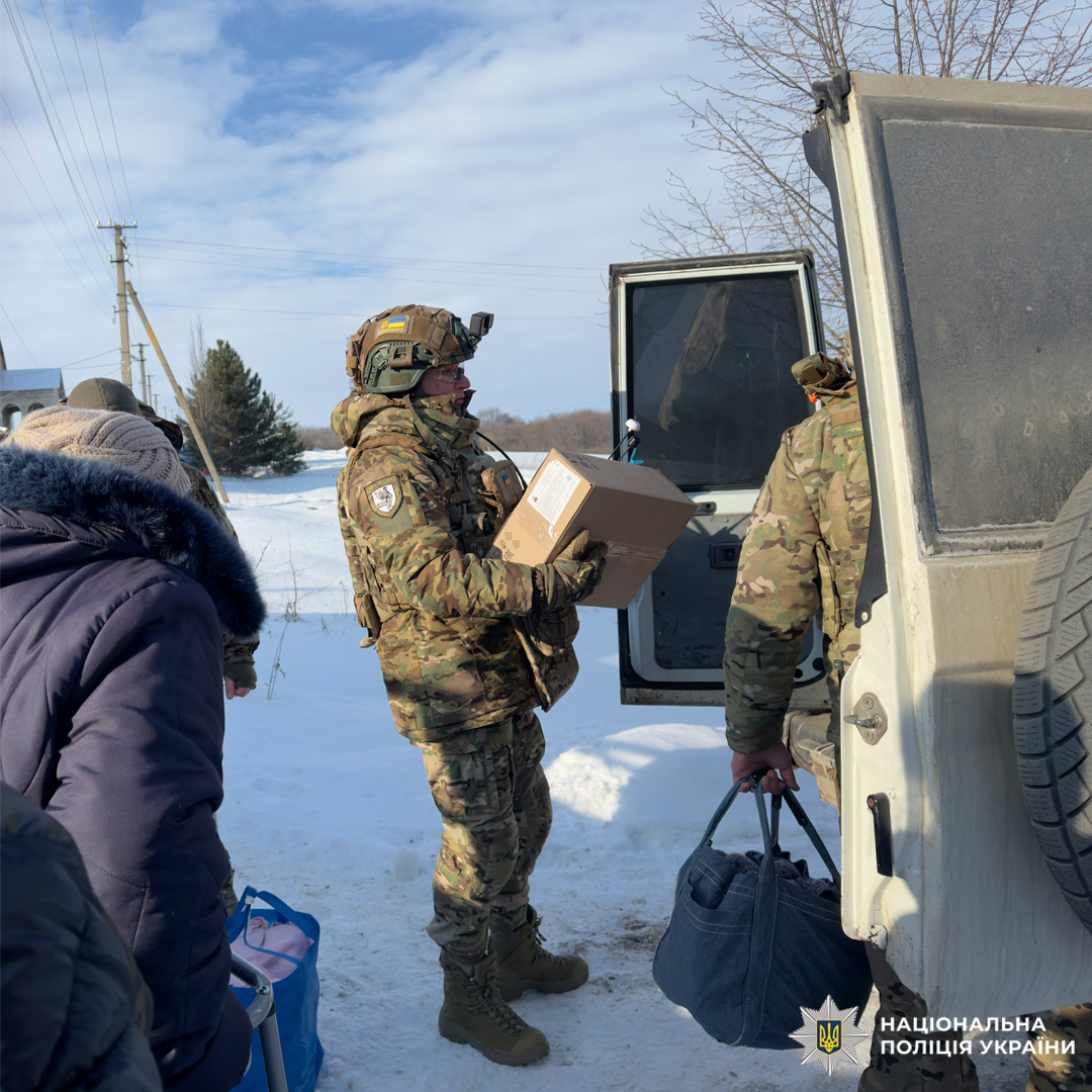Поліцейські у камуфляжній формі допомагають роздавати гуманітарну допомогу літній людині з ходунками.