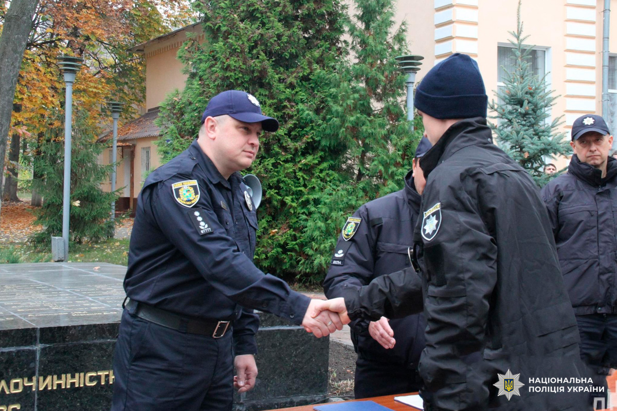 Двоє офіцерів Національної поліції України тиснуть руки під час урочистої події на відкритому повітрі.