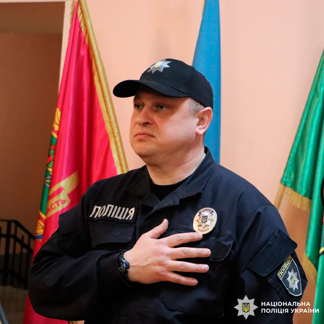 Офіцер Національної поліції України стоїть у формі з рукою на серці.