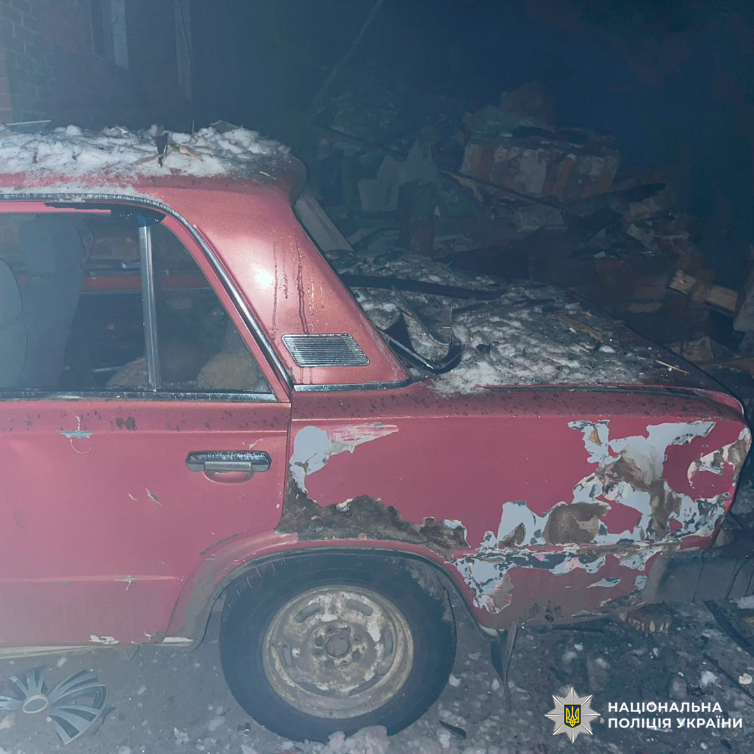 Пошкоджений червоний автомобіль зі слідами іржі та відсутнім заднім склом, вкритий снігом, поруч із купою цегли.