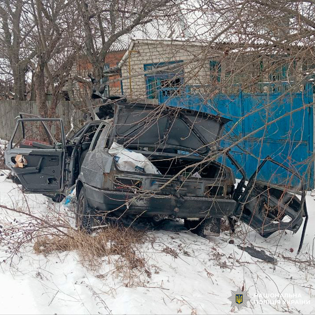 Сильно пошкоджений автомобіль із відкритими дверима стоїть серед снігу біля житлового будинку з синіми воротами.