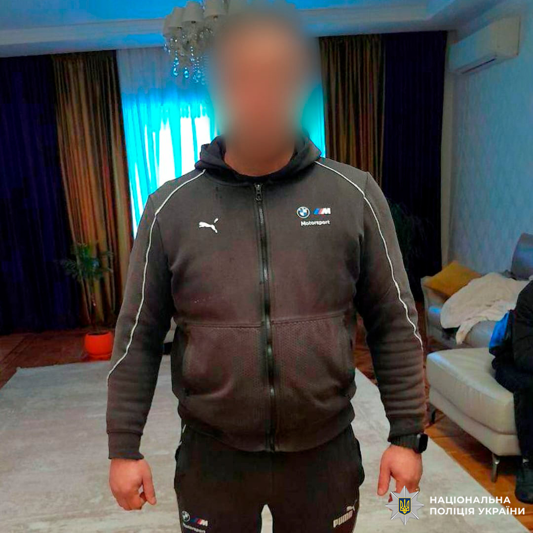 Особа у спортивному костюмі Puma з логотипом BMW Motorsport стоїть у кімнаті з меблями та рослиною, обличчя розмите.