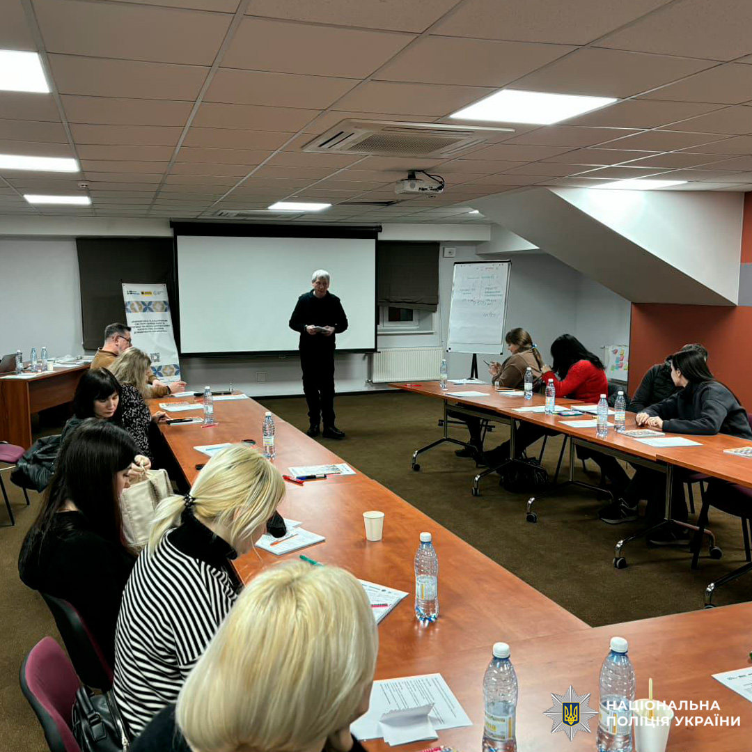 У конференц-залі проходить навчальна сесія за участю представників Національної поліції України. Люди сидять за столами у формі літери «П», слухаючи доповідача біля екрану з презентацією.