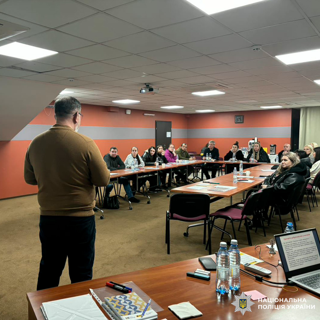 У конференц-залі проходить навчальна сесія за участю представників Національної поліції України. Люди сидять за столами у формі літери «П», слухаючи доповідача біля екрану з презентацією.
